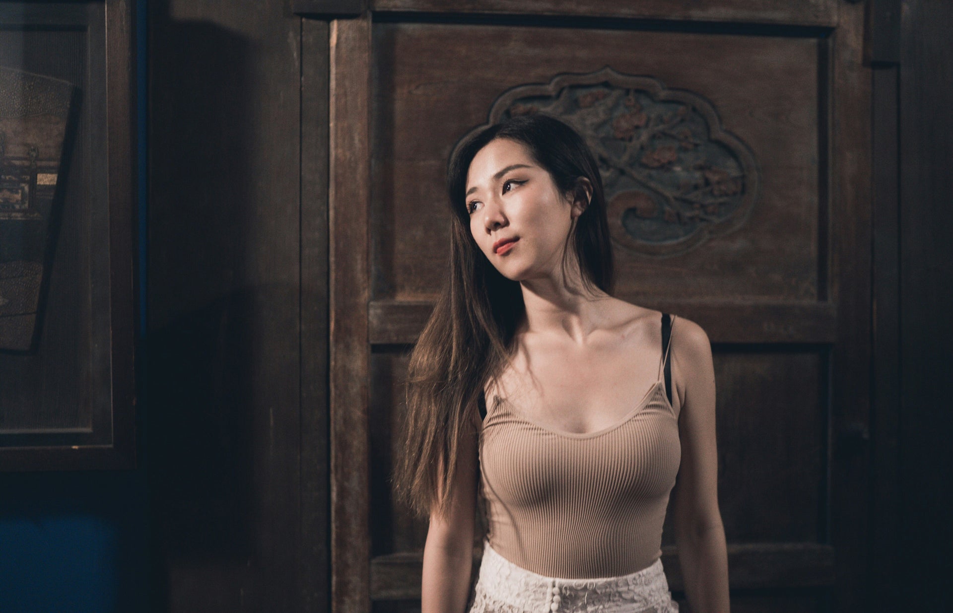 Woman in a beige top and white pants standing in front of a wooden door.