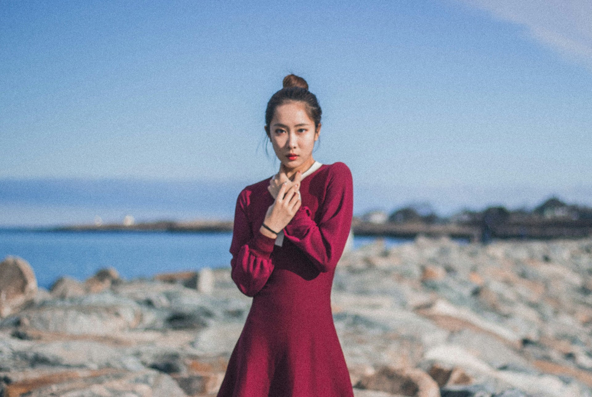 Woman in a red dress standing on rocky terrain with water in the background